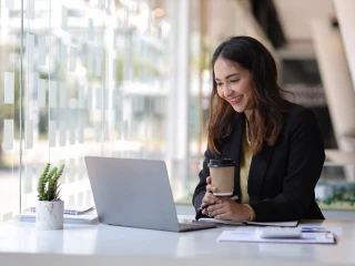 young lady holding a coffee cup smiles at laptop