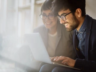A smiling man wearing glasses and a smiling lady wearing glasses working